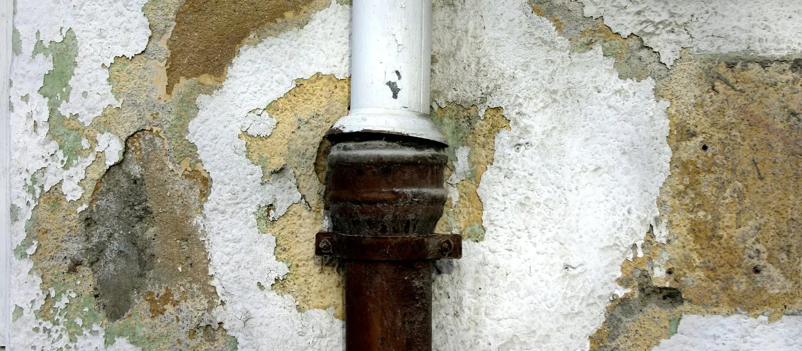 Stained and flaking wall plaster around a pipe