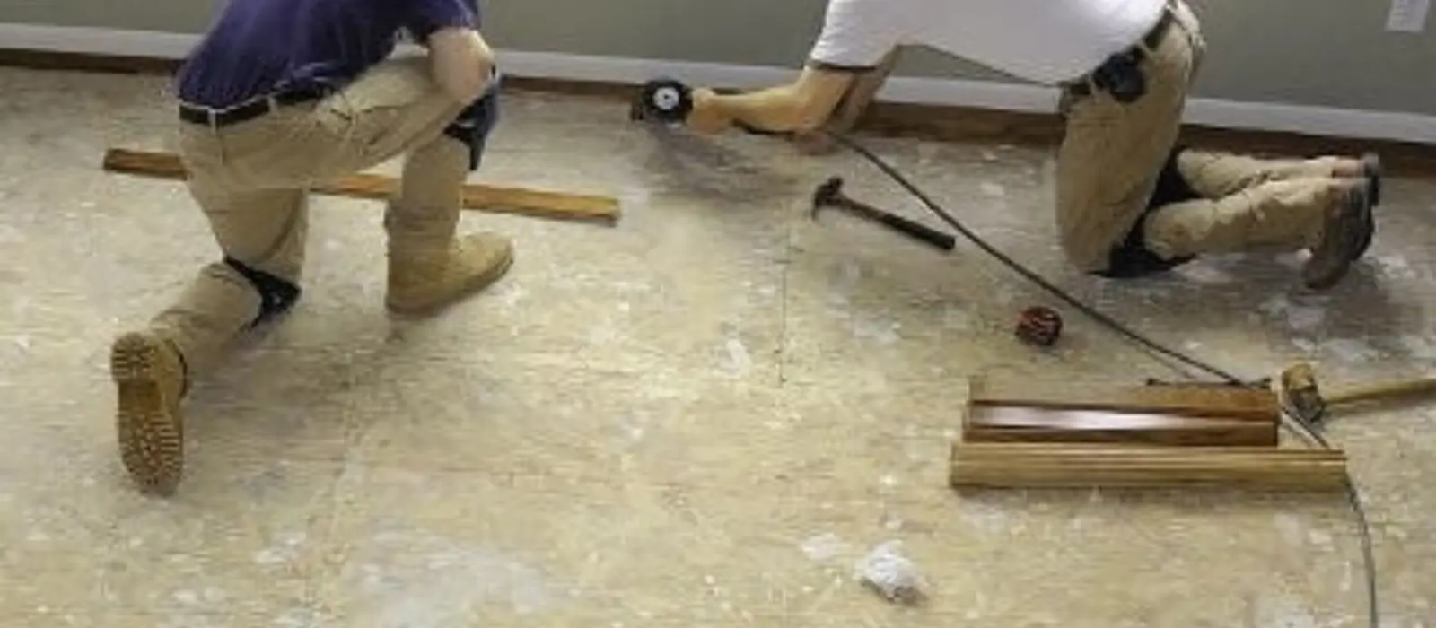 Two workers kneeling on a subfloor while installing new flooring